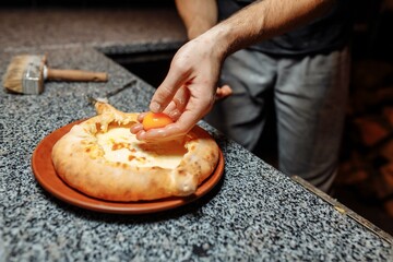 Baker hands preparing khachapuri on kitchen table. cook making traditional georgian treat with raw dough and egg. recipe concept