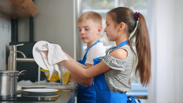 Brother And Sister Kids In Apron Washing Dishes In Modern Home Kitchen