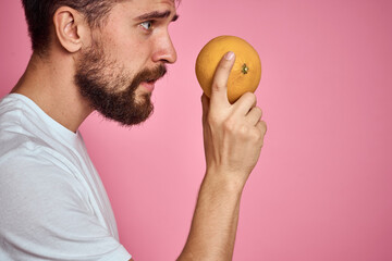Young man with orange on a pink background in a white t-shirt emotions fun gesticulating with model...