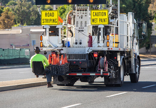 Piant striping truck with seat at the back bumper where a worker sits and places traffic cones onto the street. The truck also has an electonic traffic directional arrow