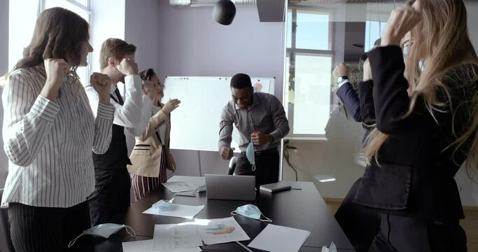 Happy coworkers business persons take off medical mask, end of pandemic. Group of colleague managers sit at office work place, read good news in net, rejoice celebrating recovery, stop corona virus