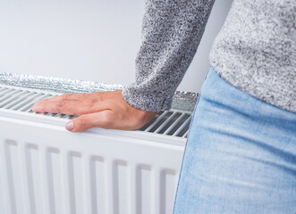 Female hand on the heating white radiator at home. The symbolic image of the heating season at...