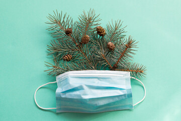Medical mask with spruce branches in it on the light green background. Christmas medical flat lay for medicine, pharmacy, and hospitals. Medical greeting card.