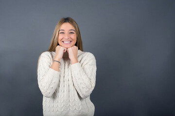 Beautiful blonde young woman wearing white sweater feeling confident against gray studio background.