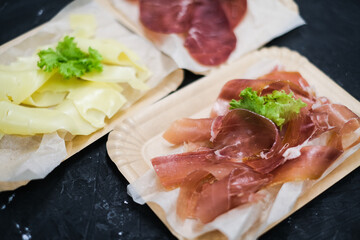 Cheese slices. Meat smoked jerky - raw meat sausage meat. Close up view on tasty sliced Chicken basturma on paper plate on a wooden background . Beer snack. Pastirma
