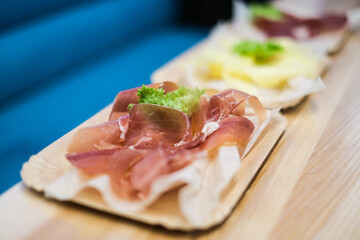 Cheese slices. Meat smoked jerky - raw meat sausage meat. Close up view on tasty sliced Chicken basturma on paper plate on a wooden background . Beer snack. Pastirma