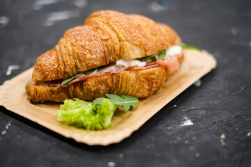 Croissant with ham and cheese arugula and lettuceon, in a paper plate top view