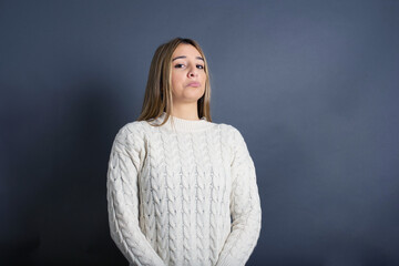 Beautiful young blonde woman wearing white sweater standing against gray background, 