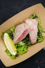 Tuna steak on a salad pillow with a slice of lemon in a paper plate