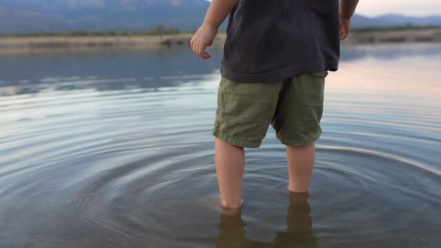 Close up of the low section of a 3 year old Caucasian boy barefoot in the cold water of a natural cove with stones and gravel