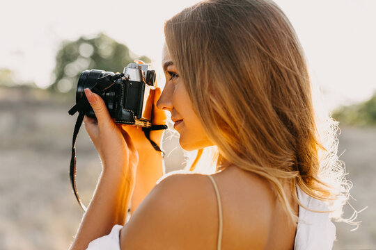 Young woman with a camera, taking pictures, outdoors in a park.