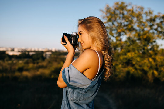 Young blonde woman with a camera, taking pictures outdoors in a park.