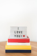 White lightbox with I love you message and a red heart on a pile of books. White background.