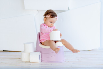 little girl sitting in a white room on a potty in pink clothes with toilet paper