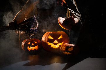 Witch casts a spell on a steaming pumpkin in the dark on Halloween