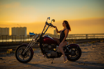 Red-haired woman in sexy lingerie in high heels sits on a motorcycle. Attractive red-haired girl sits on a motorcycle at sunset