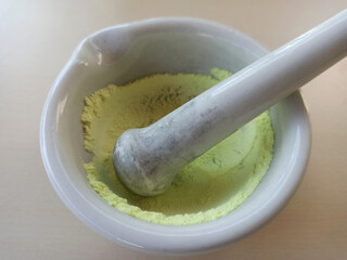 The process of grinding yellow sulfur into powder in a ceramic mortar using a pestle.