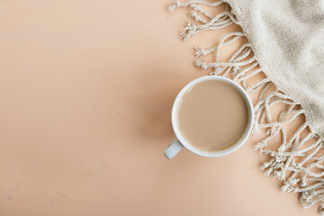 Cup of coffee with pastel beige plaid on wooden background. Autumn or winter composition. Top view, flat lay, copy space