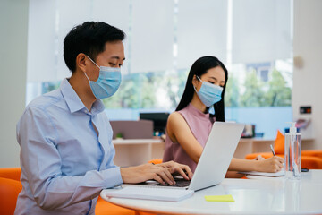 Two business coworkers sitting at table wearing protective Covid face coverings, new normal, protection, health, safety