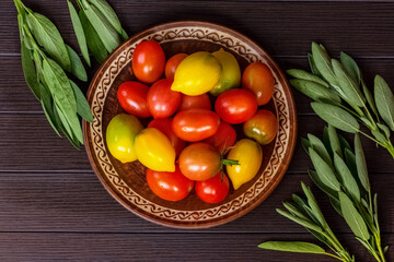 fresh red, yellow and green tomatoes in a plate on a wooden background top view. fresh ripe tomatoes and sage branches on the table view above.