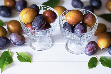 ripe purple and yellow plums in glass bowls on a white background. plums on the table close-up. background with fresh plums.