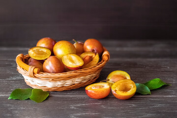 ripe yellow plums in a wicker basket on a wooden background close-up. whole plums and half plums on the table and copy space. background with yellow plums.