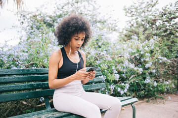 Focused young sportswoman listening to music on smartphone in garden