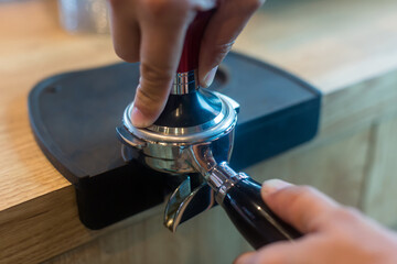 Barista pressing coffee in the machine holder. Coffee powder on coffee tamper. barista using tamper to press ground coffee into portafilter to make espresso hot drink.