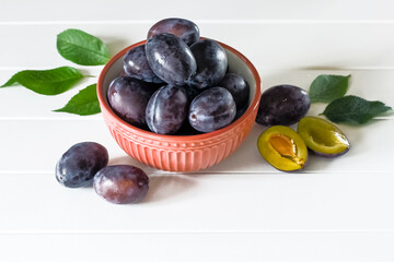 ripe blue plums in a wooden bowl standing on sacking. background with whole plums and half plums. plums in a bowl close-up.