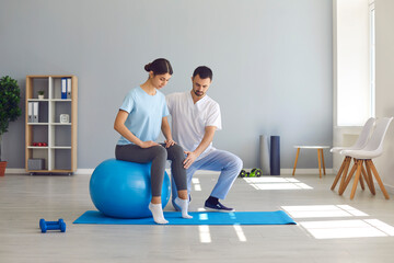 Man doctor chiropractor fixing woman on fitness ball in right position for pain relief