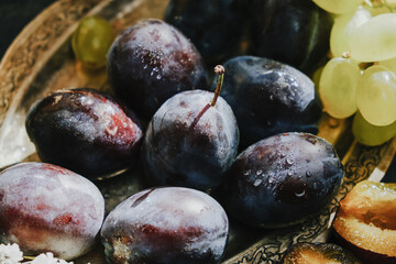 Fototapeta premium Plums and white grape on silver platter. Fruits still life.