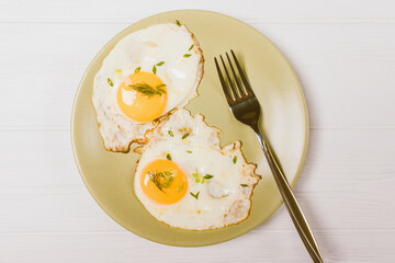 Top view of fried eggs and fork on green plate