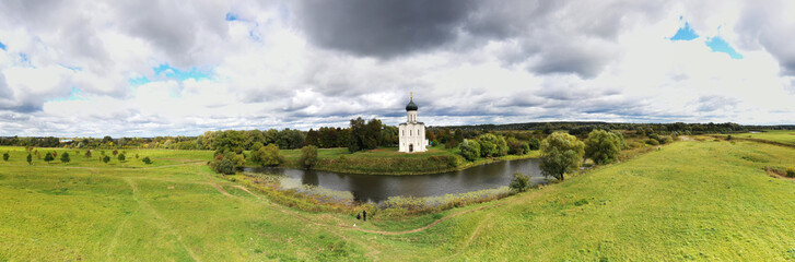 Fototapeta na wymiar a panoramic view of the white old church on a green meadow between the tributaries of the river against the backdrop of thunderclouds filmed from a drone