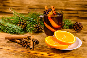 Cup of mulled wine with cinnamon, sliced orange and fir tree branches on wooden table