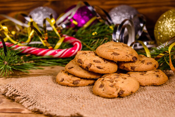 Pile of the chocolate chip cookies on sackcloth in front of christmas decorations