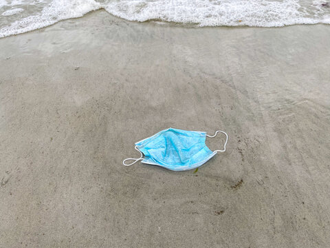 Disposable mask on beach as trash with ocean wave crashing during pandemic