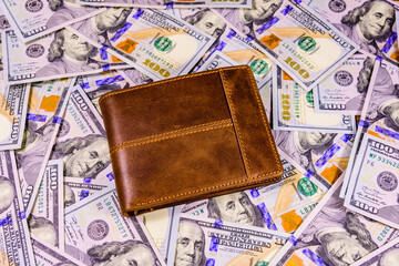 Closed brown leather wallet on the one hundred dollar banknotes