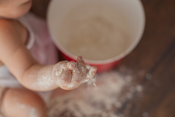 Little chef in apron and a suit of a cook, sits on a dark wooden background. She is a bakery. Close up and macro photo. 