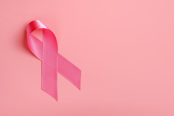 Pink ribbon on pink background. Breast cancer awareness concept, copy space, flat lay 