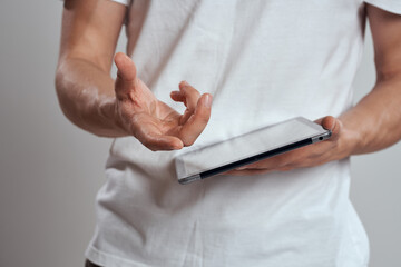 Tablet with a touch screen on a light background male hands white t-shirt cropped view