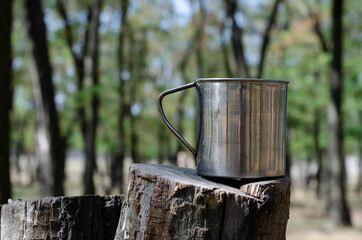 Naklejka na ściany i meble Metal mug on a tree stump in the forest.