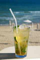 mojito cocktail in a glass glass with a straw on the background of the sea beach on a sunny day