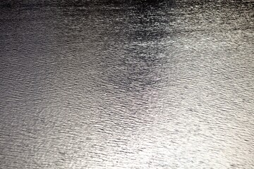 Silver surface of wavy water with bright highlights and reflections. Ripples on water surface close-up. Glowing surface of the water. Silver metal surface with highlights close-up. Abstract background