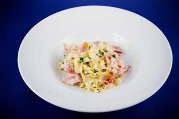 Carbonara pasta with bacon and basil on a plate.
