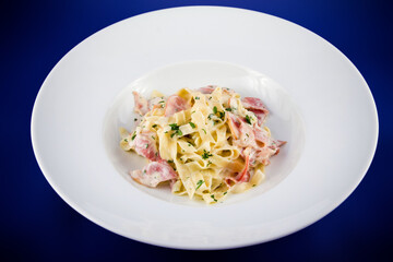 Carbonara pasta with bacon and basil on a plate.