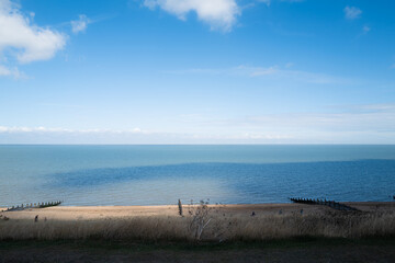Obraz premium Beautiful blue tones in the sea and sky along the sea front in Tankerton, Whitstable. There are groyne, water breakers on the beach and a windfarm with turbines on the horizon.