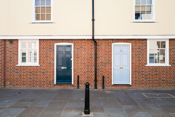 Two front doors, one dark blue, one light blue, on a modern terrace town house with brick lower...