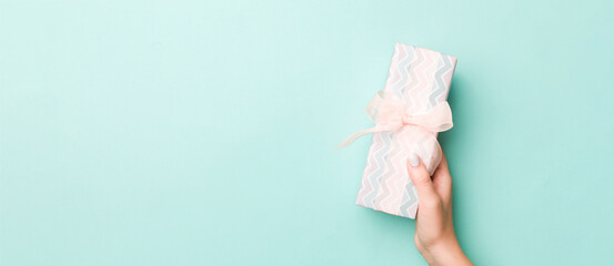 Woman hands give wrapped christmas or other holiday handmade present in colored paper. Present box, decoration of gift on Blue table, top view with copy space