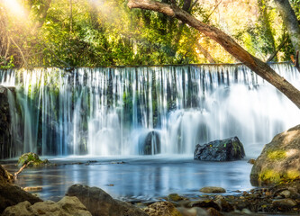 Natural waterfall called “Cascada del Hervidero” in Madrid, in the forest, with sunlight between vegetation and rocks. 