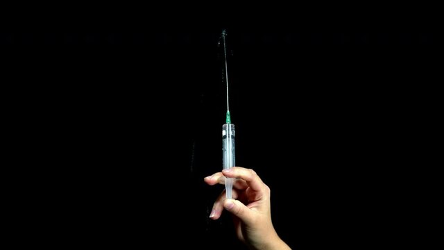 On a black background, a hand holds a syringe and squeezes out liquid from it